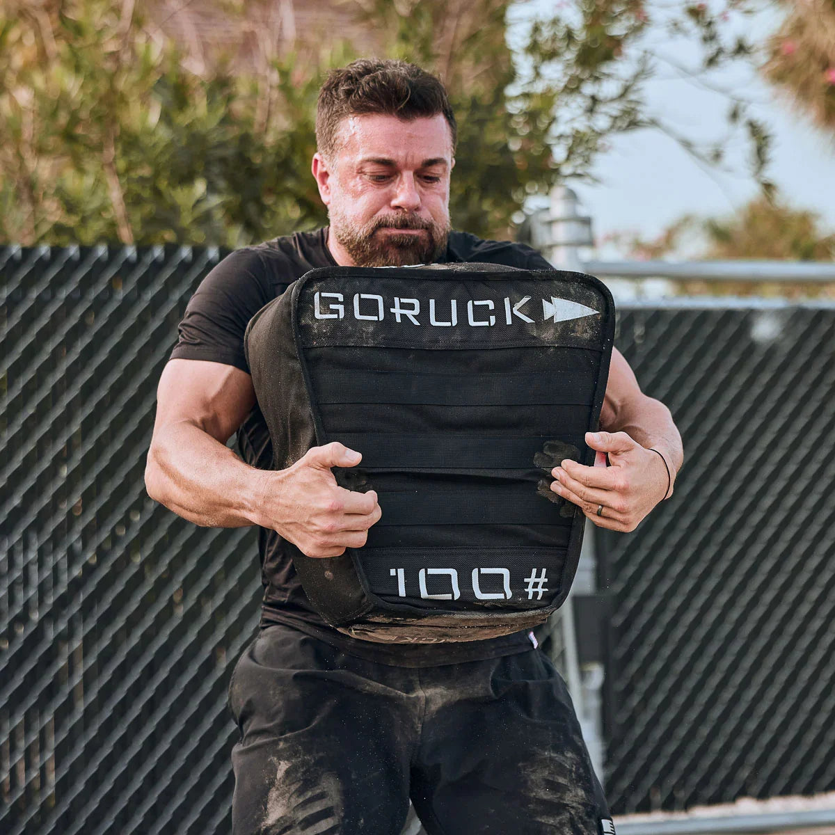 Man lifting GORUCK 100 lb sand tombstone, outdoor rucking gear workout