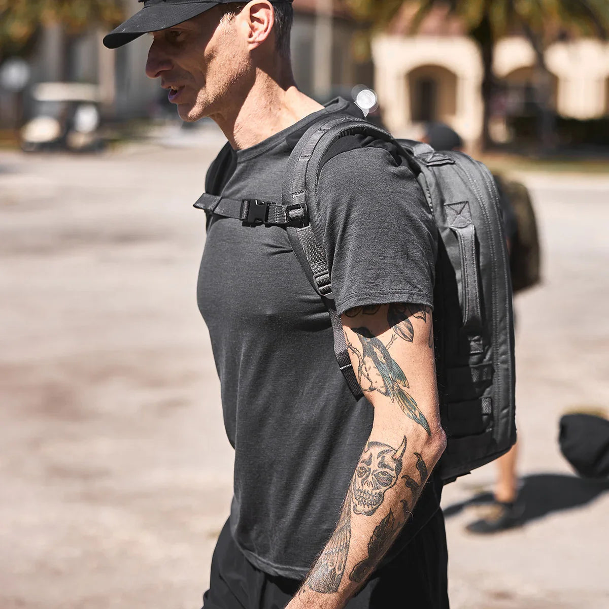 Man wearing a GORUCK grey backpack with sternum strap outdoors, visible arm tattoos