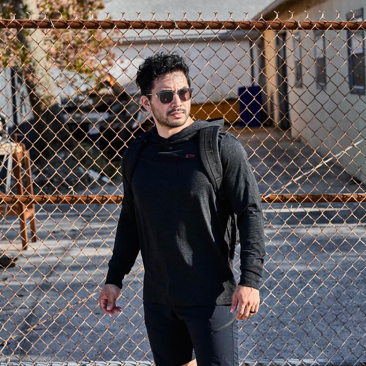 Man wearing GORUCK black hoodie and rucksack outdoors near chain-link fence