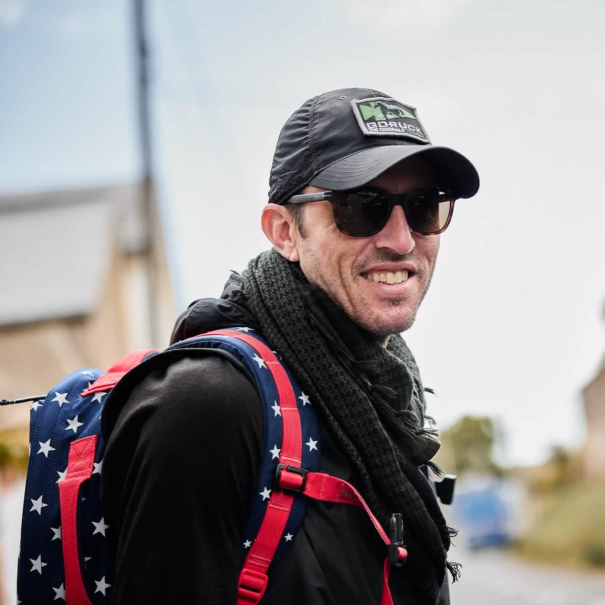 Man wearing GORUCK hat, sunglasses, and star-pattern rucksack outdoors
