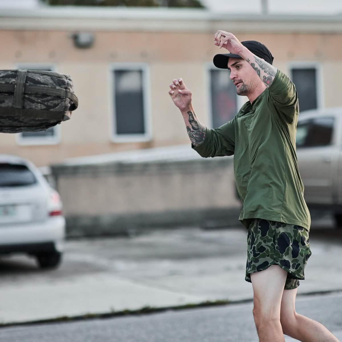 Man in green GORUCK Tough Mesh Hoodie lifting sandbag outdoors, rucking gear demonstration
