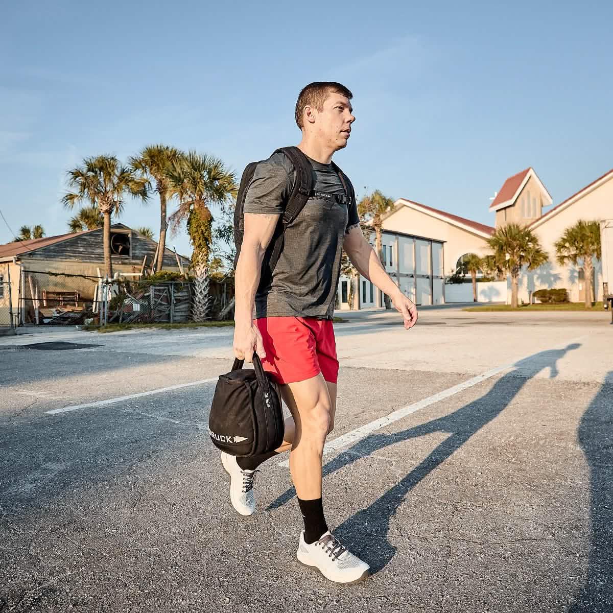 Man rucking outdoors with GORUCK backpack and gym bag, wearing athletic gear
