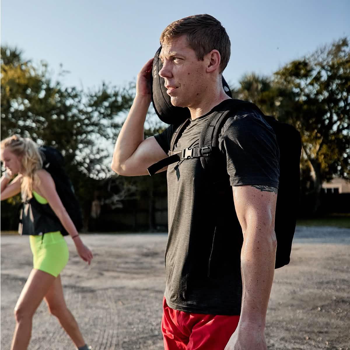 Two athletes rucking outdoors with GORUCK gear, carrying sandbags and backpacks