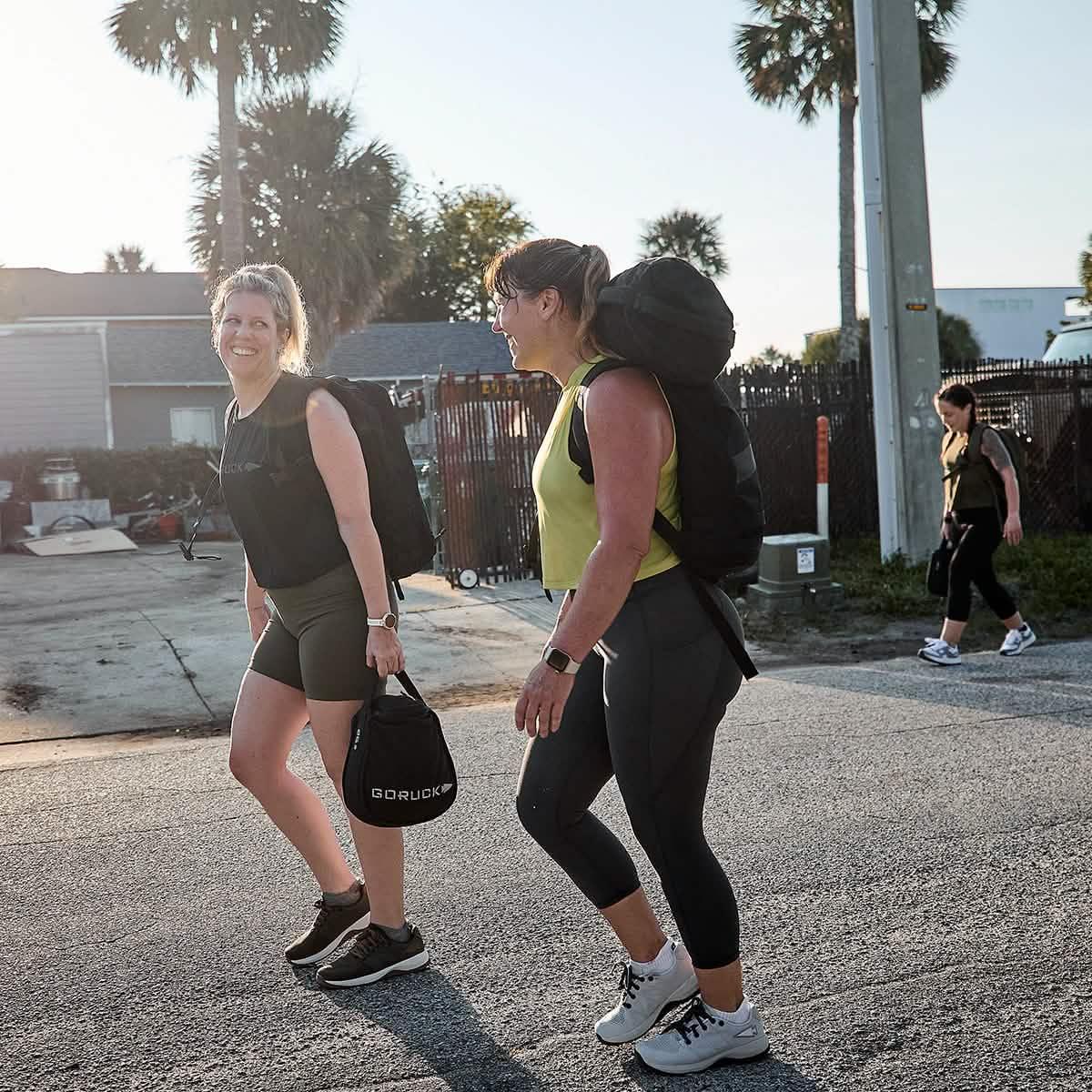 Women rucking outdoors wearing GORUCK gear and Ballistic Trainers, walking on a sunny street.