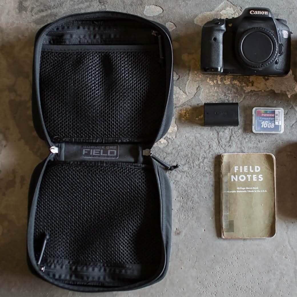 GORUCK Field Pouch open on concrete with camera, SD card, battery, and notebook gear layout
