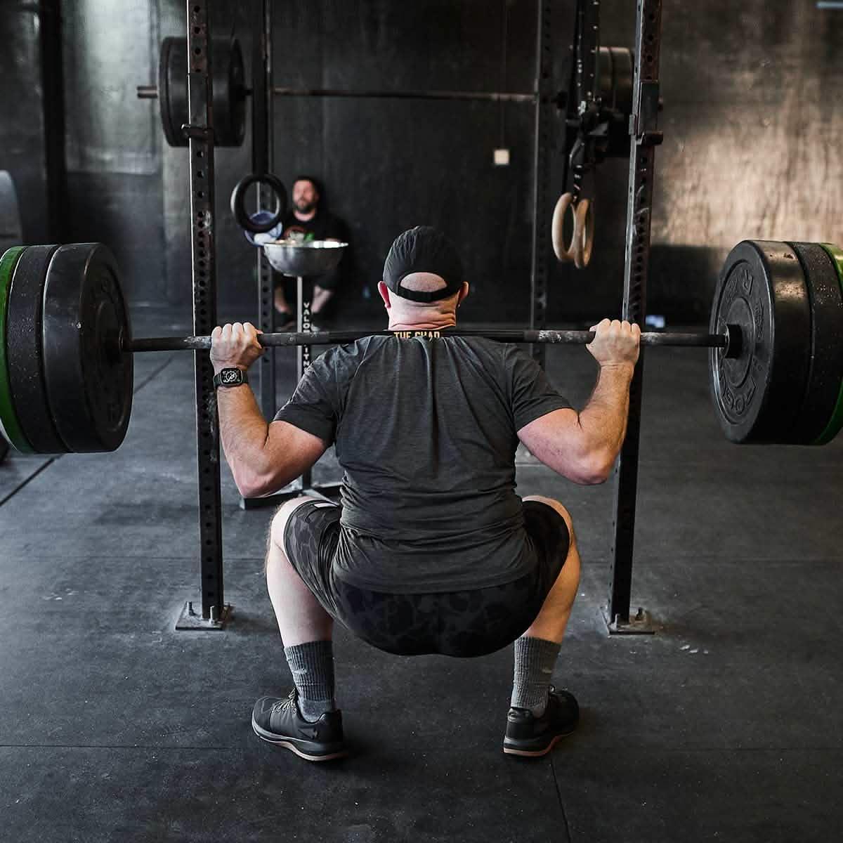 Man performing barbell squat in gym with black GORUCK rucking gear and weight plates