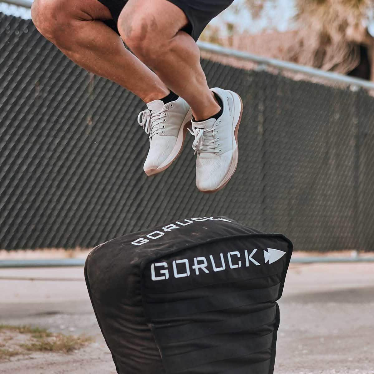 Man jumping onto GORUCK plyo box outdoors, showcasing rucking workout gear.