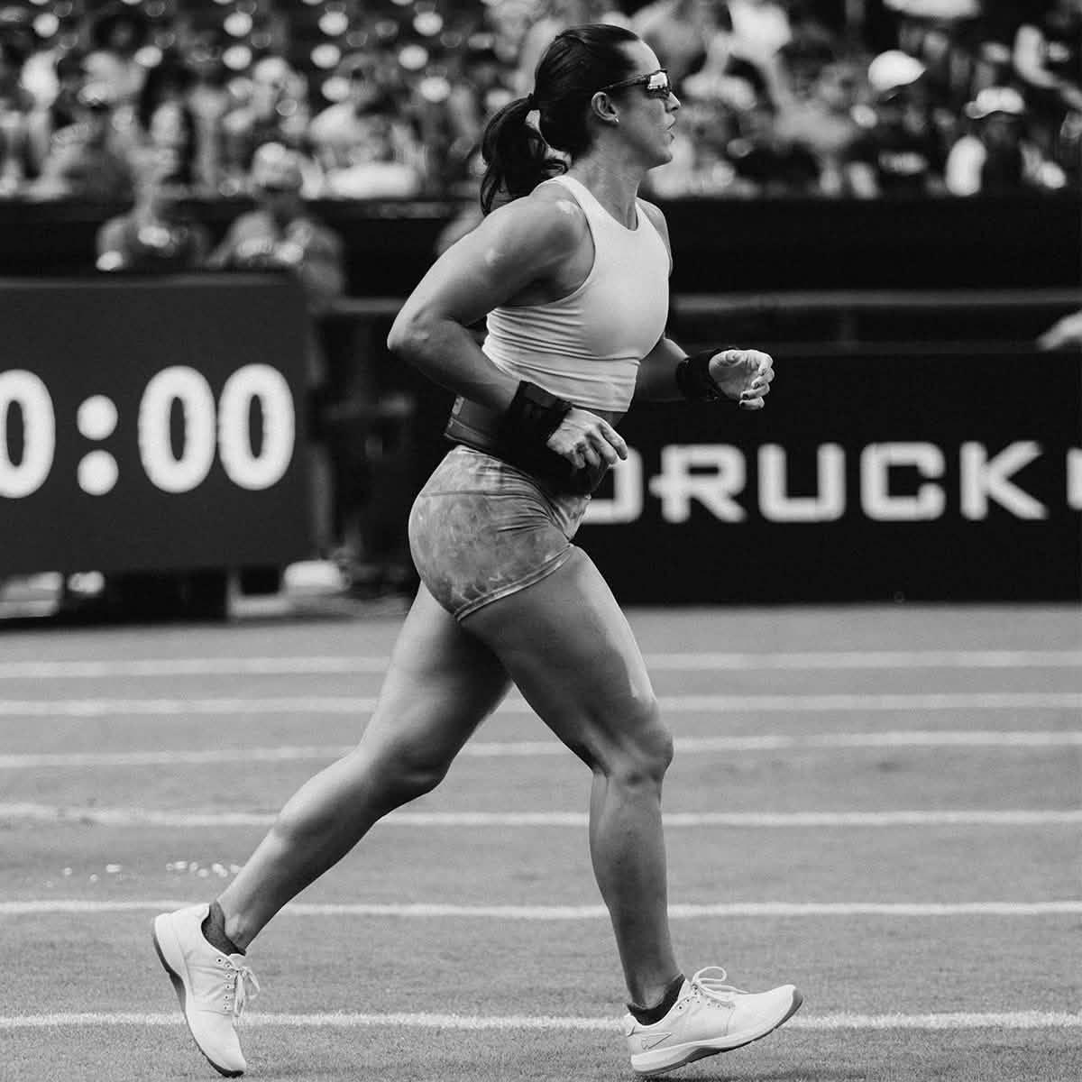 Athlete running on track in GORUCK gear during rucking event, crowd in background