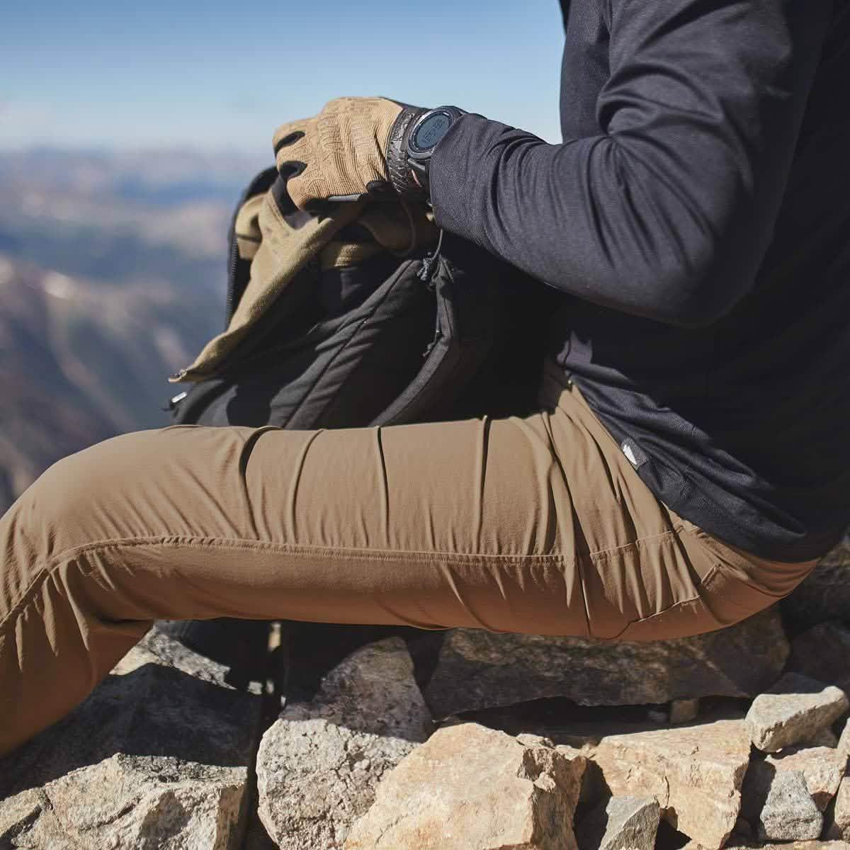 Person in GORUCK outdoor gear sits on rocks, packing a rucksack with mountain view