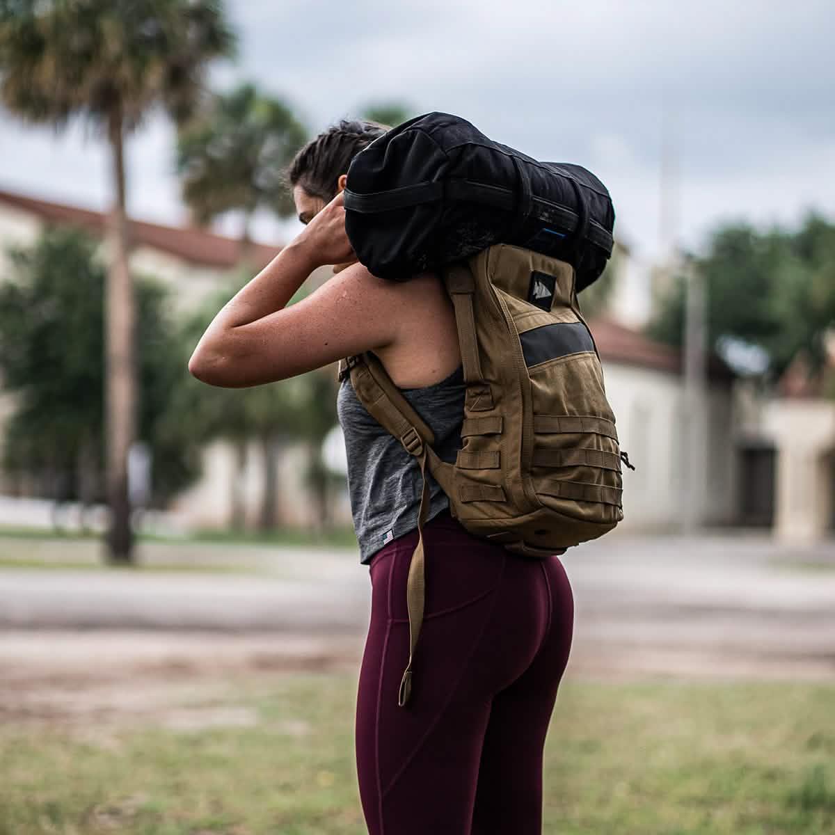 Woman outdoors rucking with GORUCK backpack and sandbag, wearing athletic gear