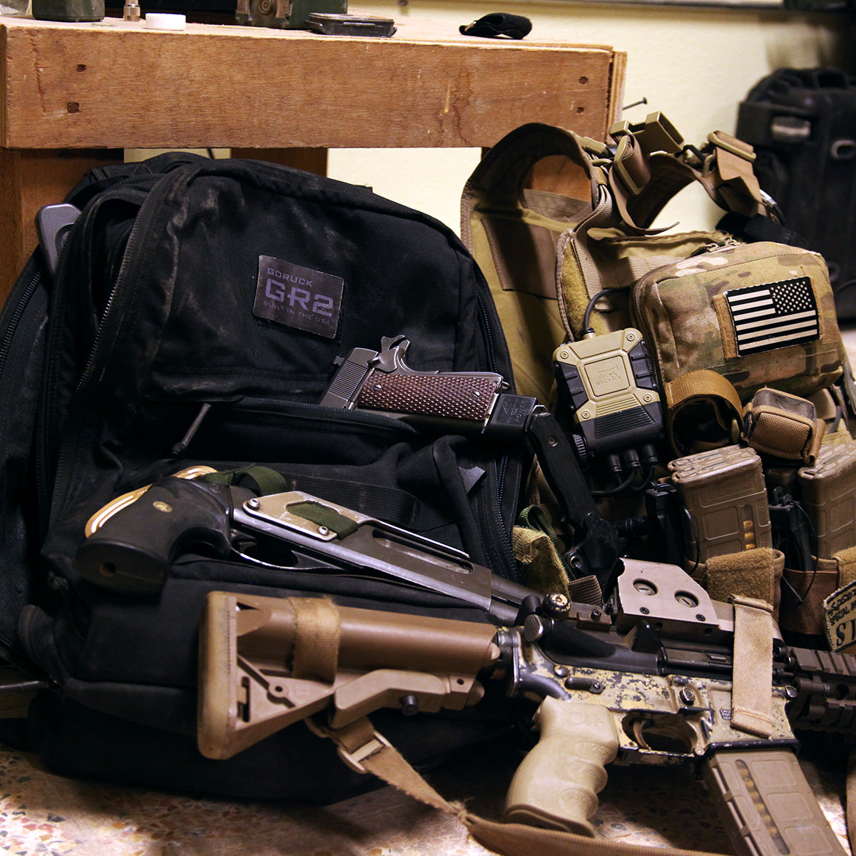 A tactical backpack, rifle, handgun, and gear with an American flag patch on a bench.