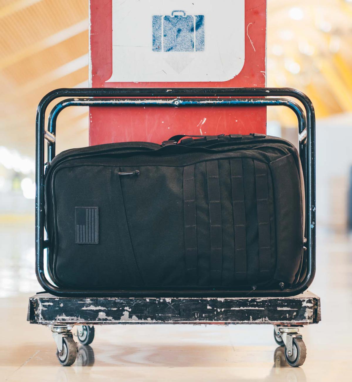 A black duffel bag sits on a luggage cart in an airport terminal.