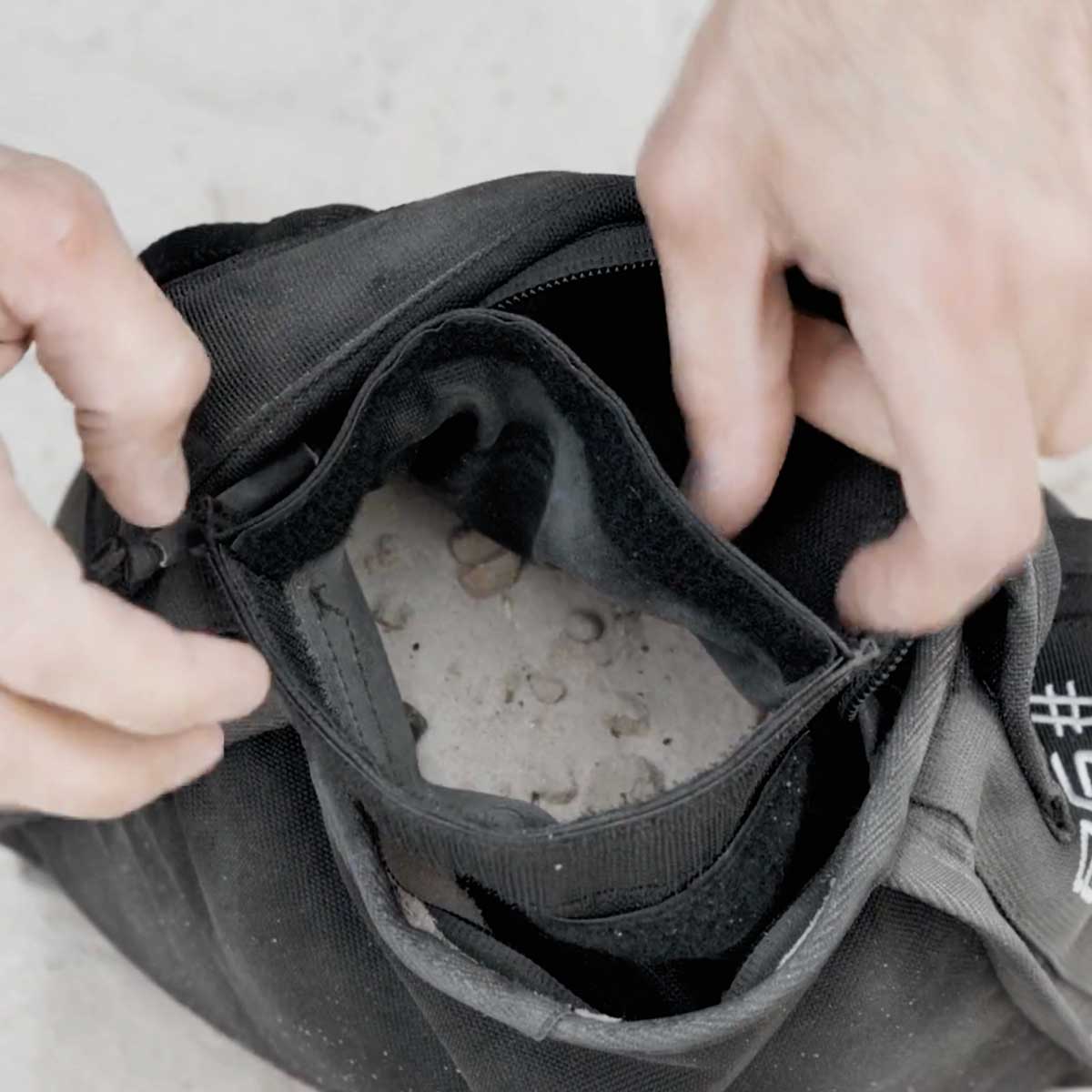 A person opens a black bag filled with sand or dirt, showing the contents inside.