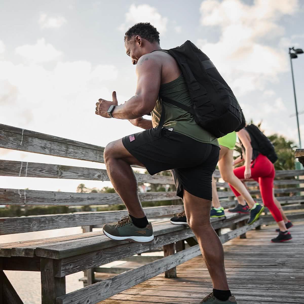 Man rucking on wooden bridge wearing GORUCK gear and backpack, leading fitness group outdoors