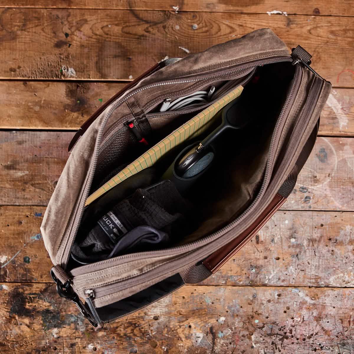 GORUCK rugged messenger bag open on wood table, packed with gear, notebook, and accessories