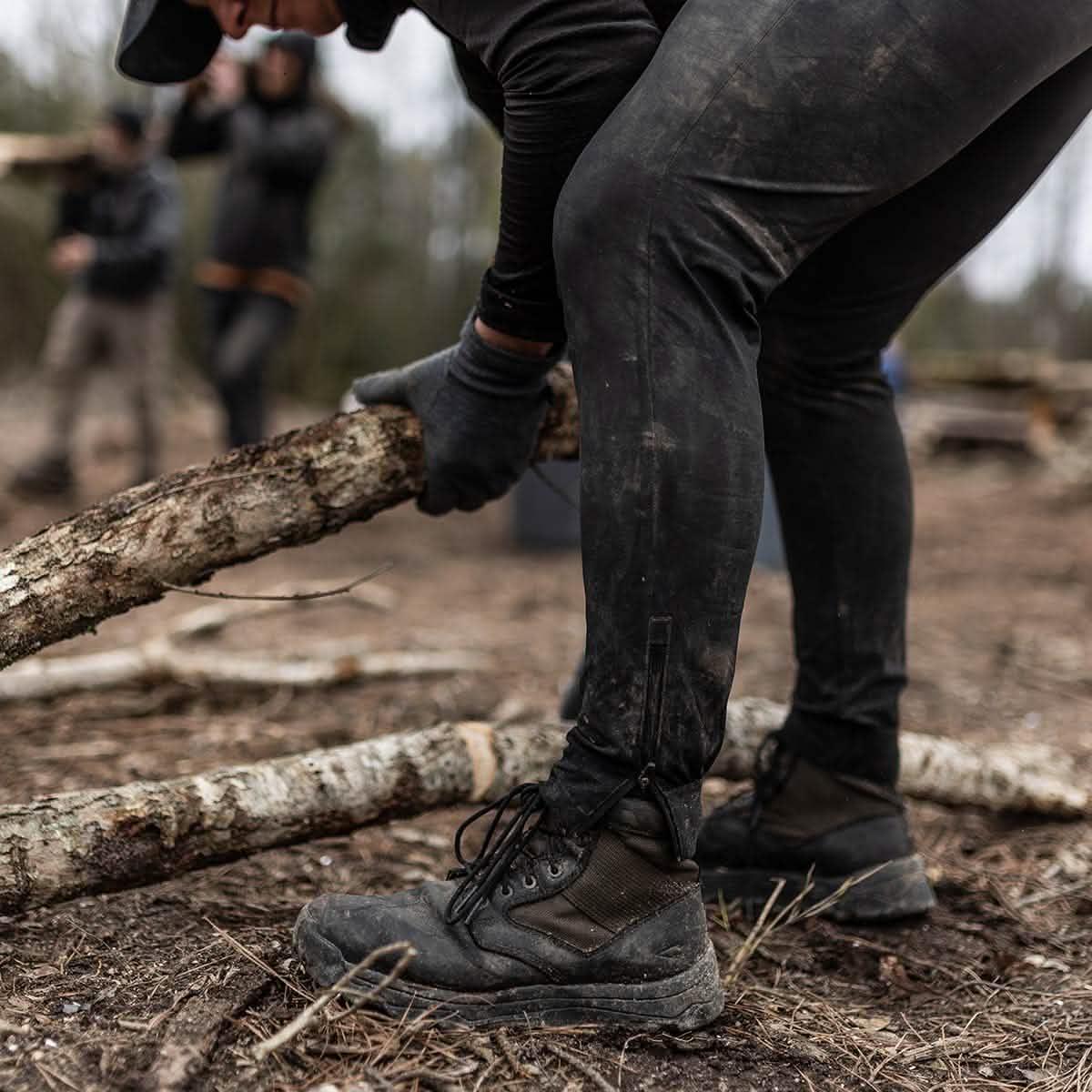 Person in rugged GORUCK boots and gloves lifting a log outdoors during rucking event