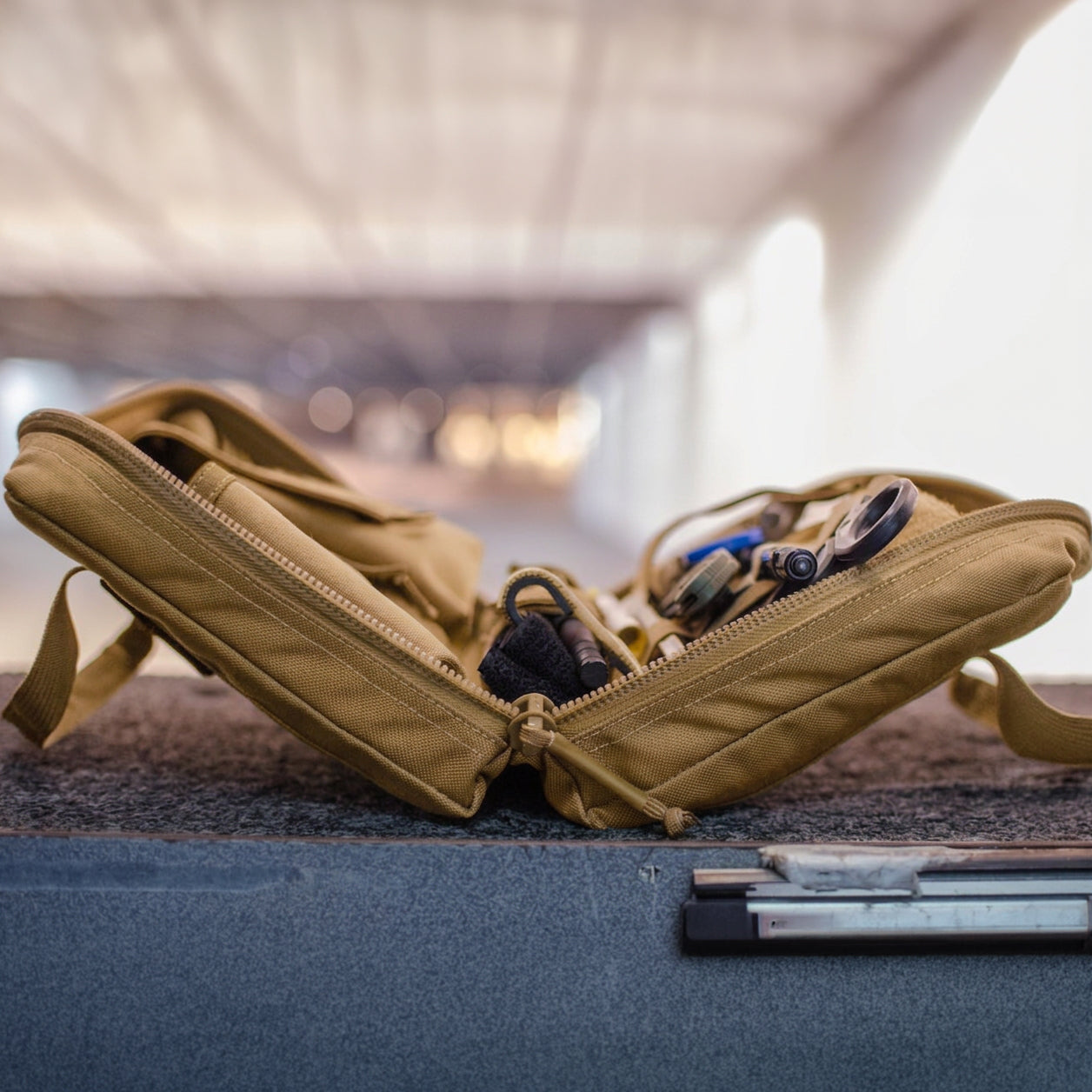 The tan Pistol Rug, unzipped on a surface, reveals organized gear inside—including a modular pistol case and magazine pouch—against a blurred background.