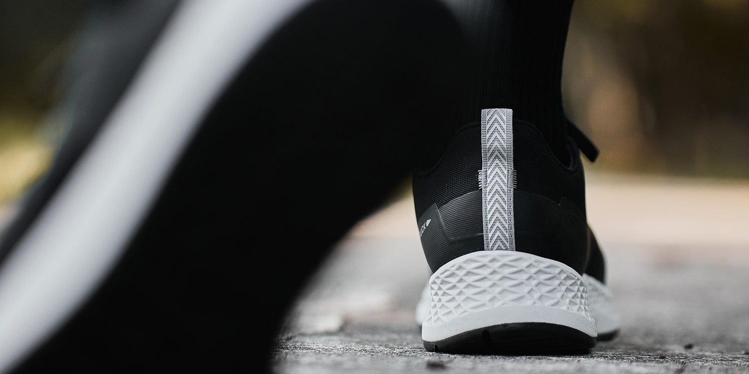Close-up of a person wearing black and white athletic shoes walking on a pavement outdoors.