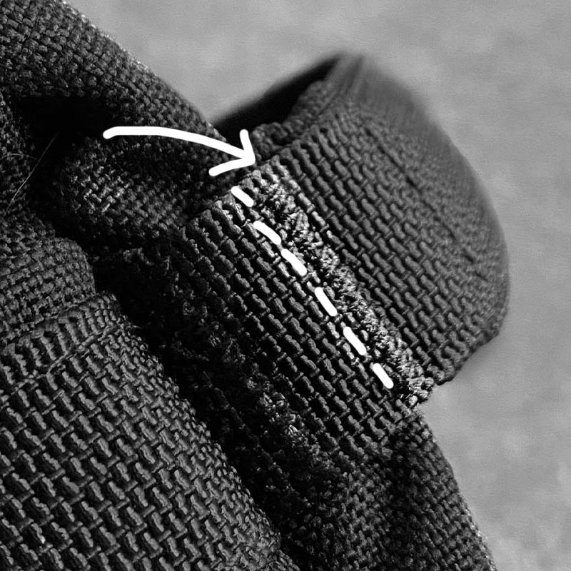 Close-up of black fabric with white stitching and a white arrow pointing to the stitches.