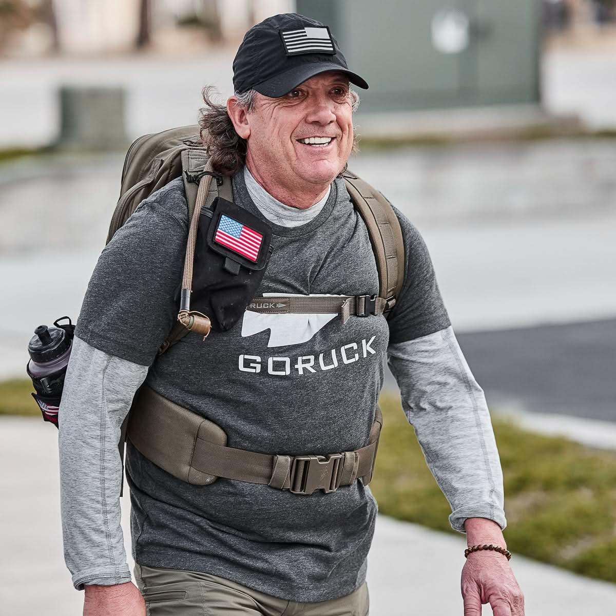 Man rucking outdoors in GORUCK Three Rules Tee, black cap, backpack, and tactical belt