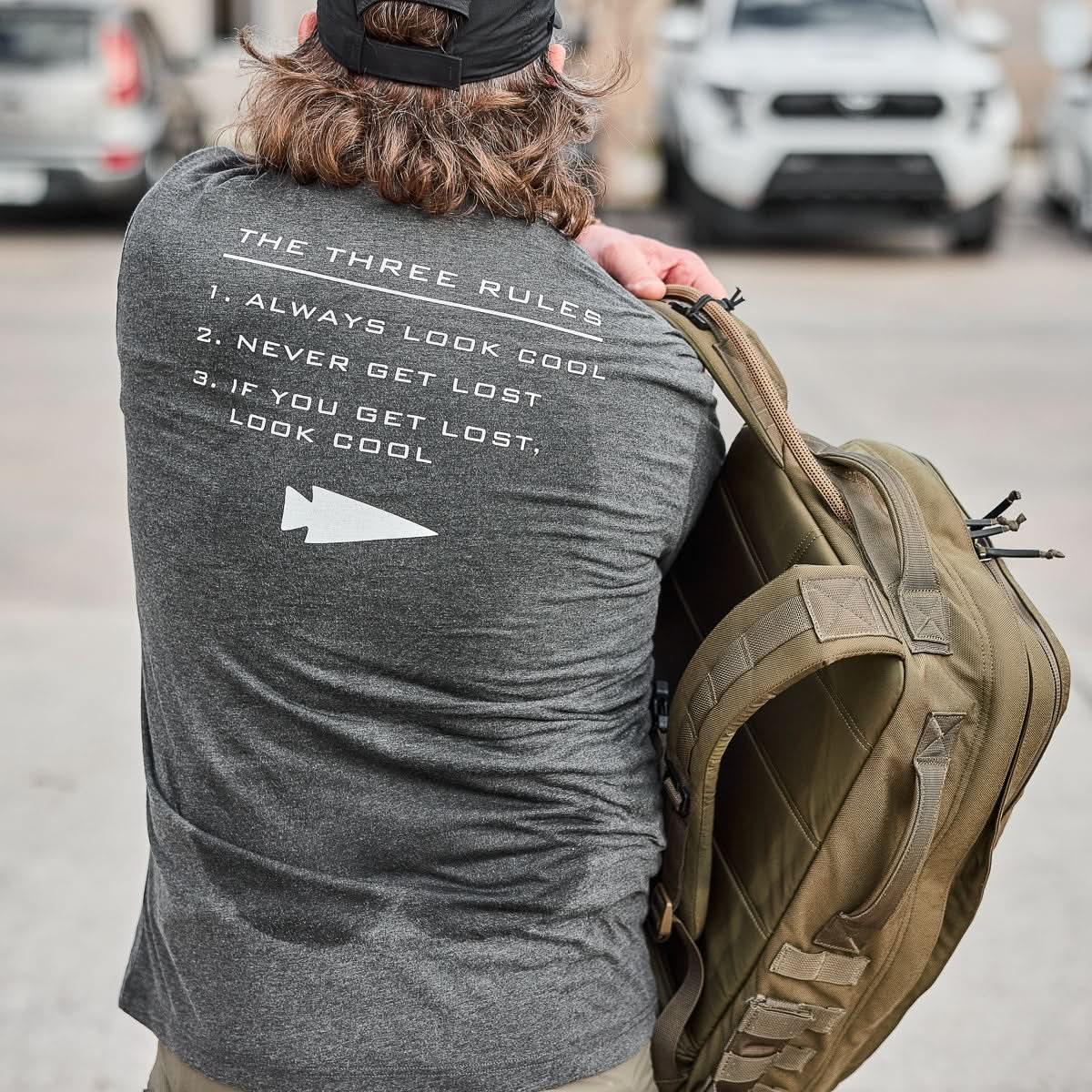 GORUCK Three Rules Tee charcoal shirt with printed rules, man holding rucksack outdoors