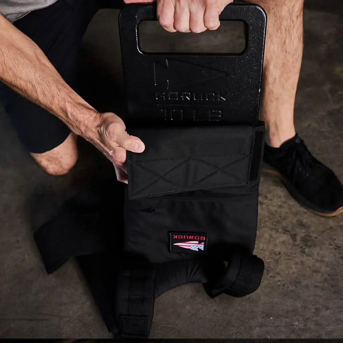 Man loading GORUCK 10LB ruck plate into a black GORUCK rucksack on concrete floor