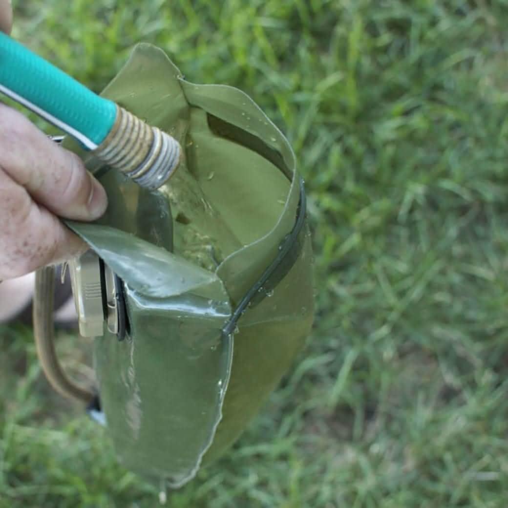 Filling a green GORUCK hydration bladder with water outdoors on grass