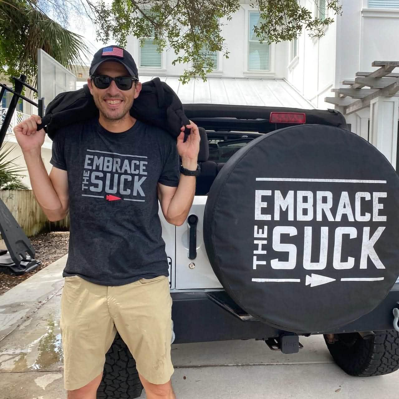 Man wearing GORUCK Embrace the Suck shirt, standing by Jeep with matching tire cover outdoors