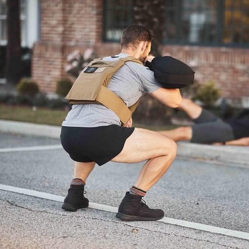 Man outdoors wearing GORUCK rucking gear, shorts, squatting with weighted pack in urban setting