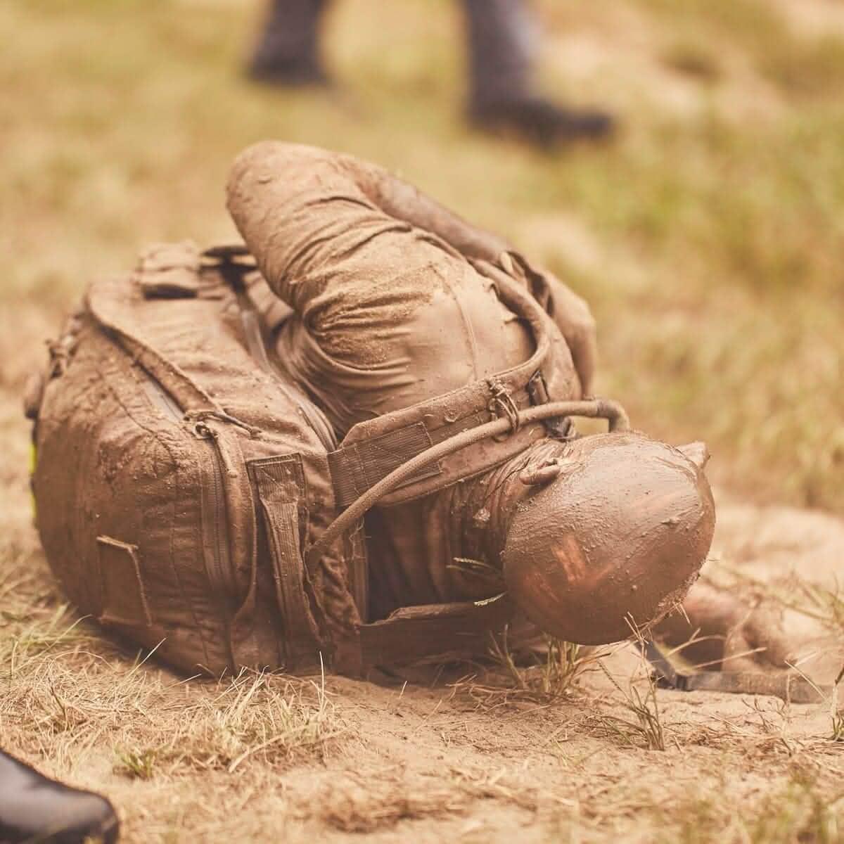 Person covered in mud crawling with a GORUCK rucksack during outdoor rucking event