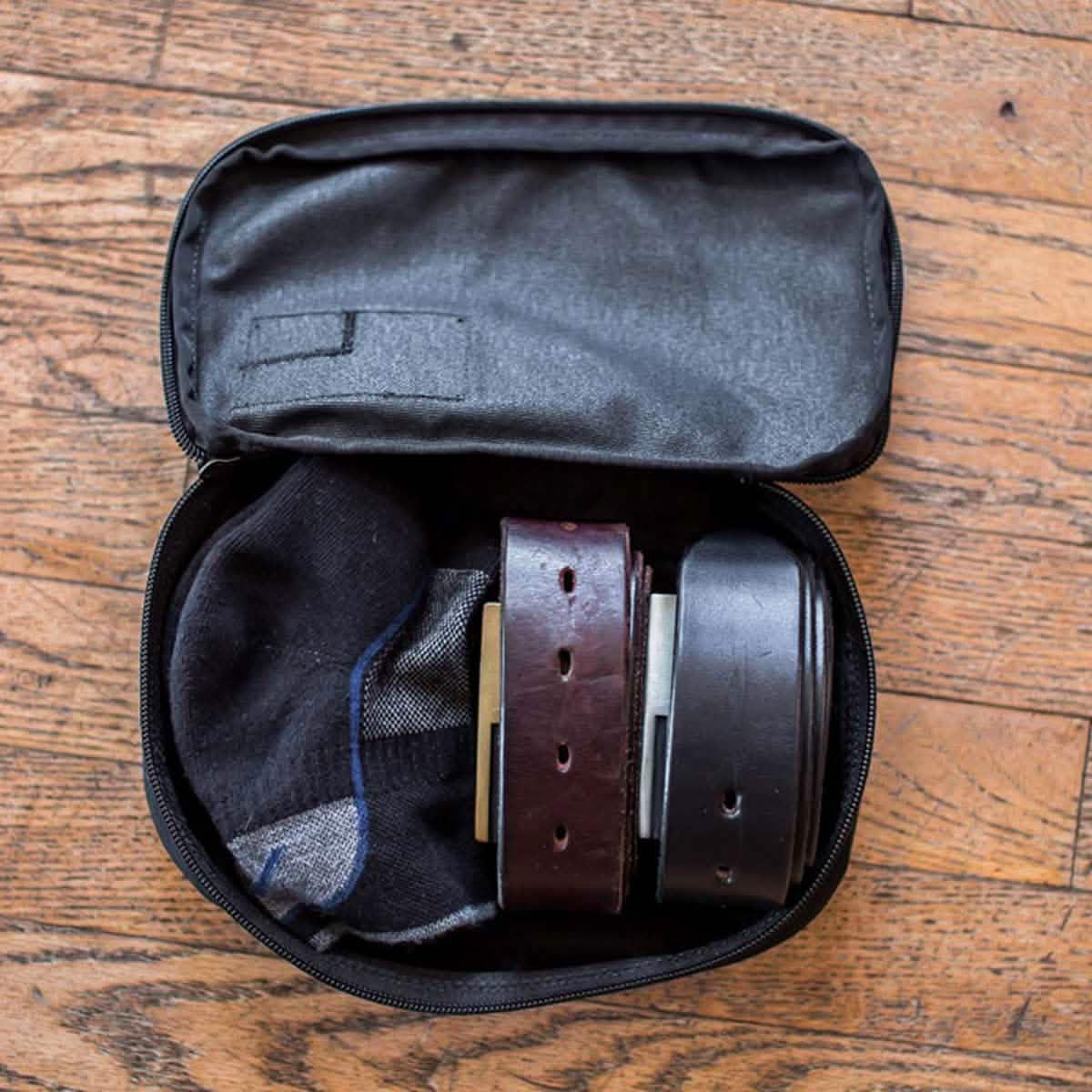 GORUCK Shadow Pocket travel pouch open with socks and belts packed inside on wood floor