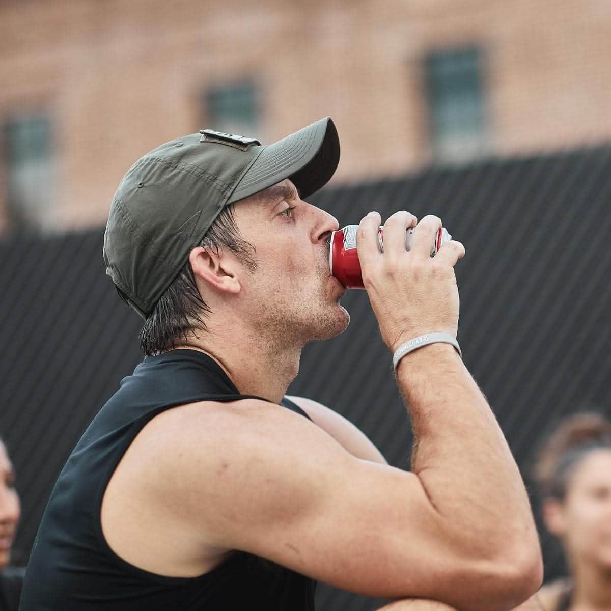 Man in GORUCK performance tactical hat drinking from can outdoors, rucking gear lifestyle
