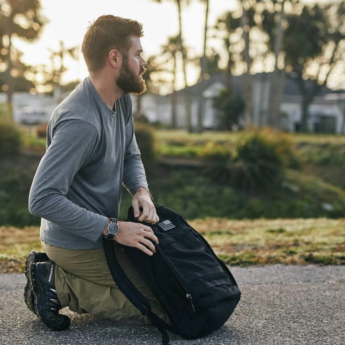 Man kneeling outdoors with a GORUCK black rucksack, preparing for rucking activity