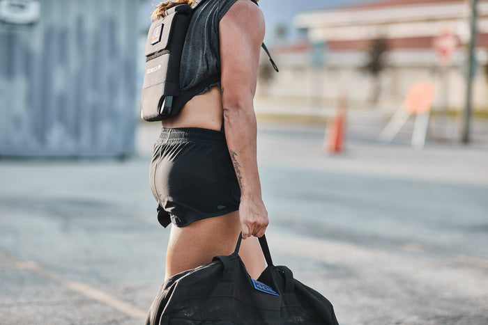 Athlete outdoors with GORUCK backpack and rucking sandbag, showcasing rugged fitness gear.