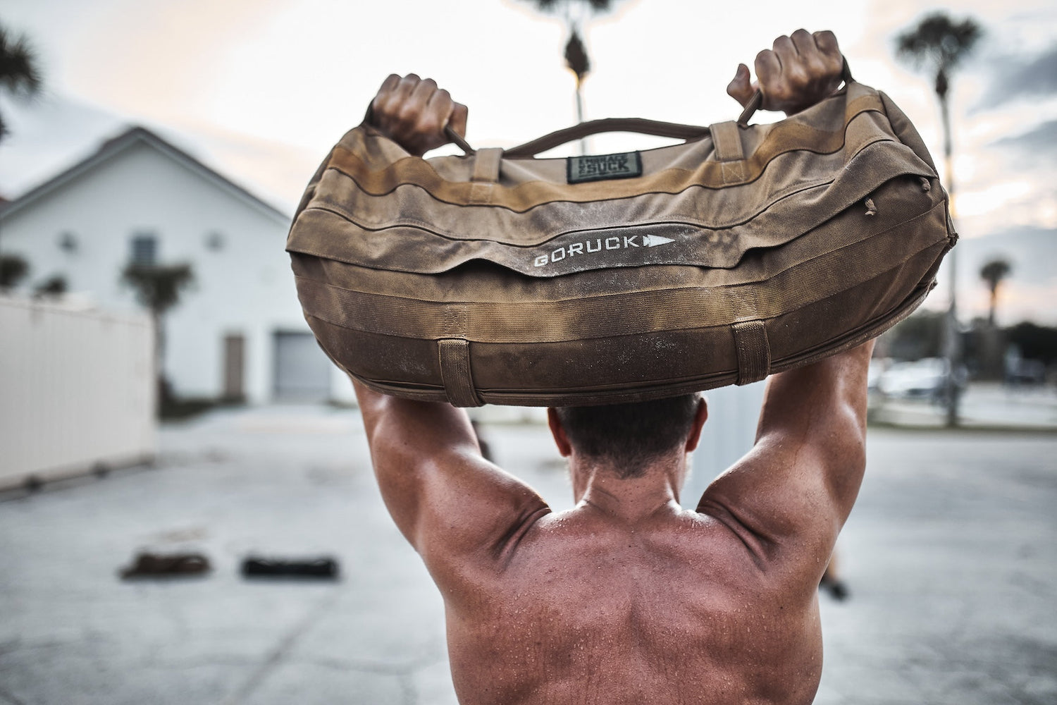 Man lifting GORUCK sandbag outdoors, showcasing rucking gear and fitness training strength