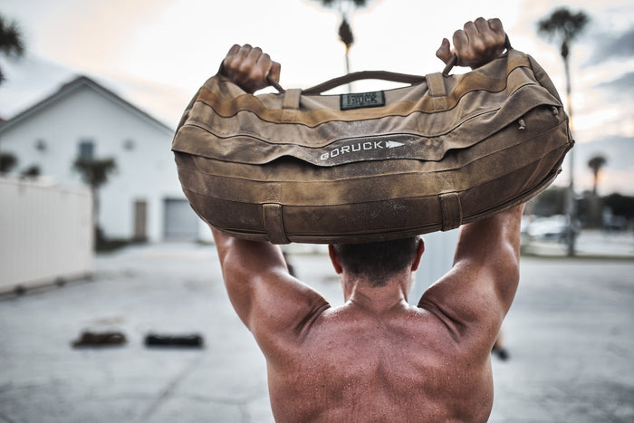 Man lifting GORUCK sandbag outdoors, showcasing rucking gear and fitness training strength