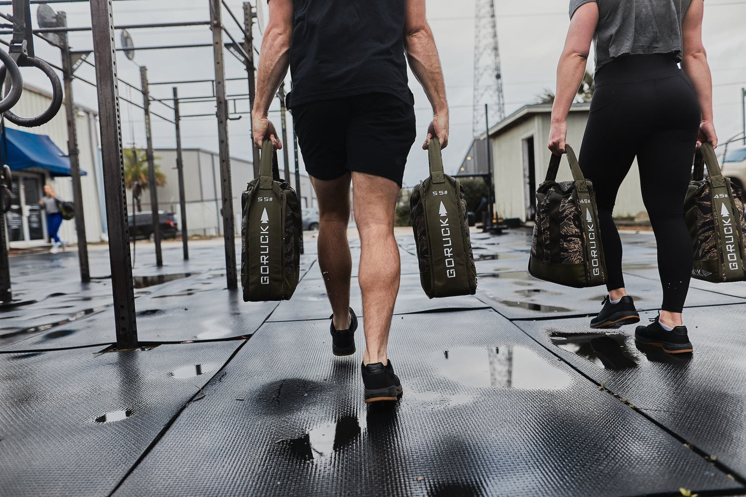 Two people rucking outdoors with GORUCK sandbags on a wet gym surface