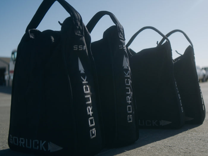 GORUCK rucking sandbags lined up outdoors on pavement in sunlight