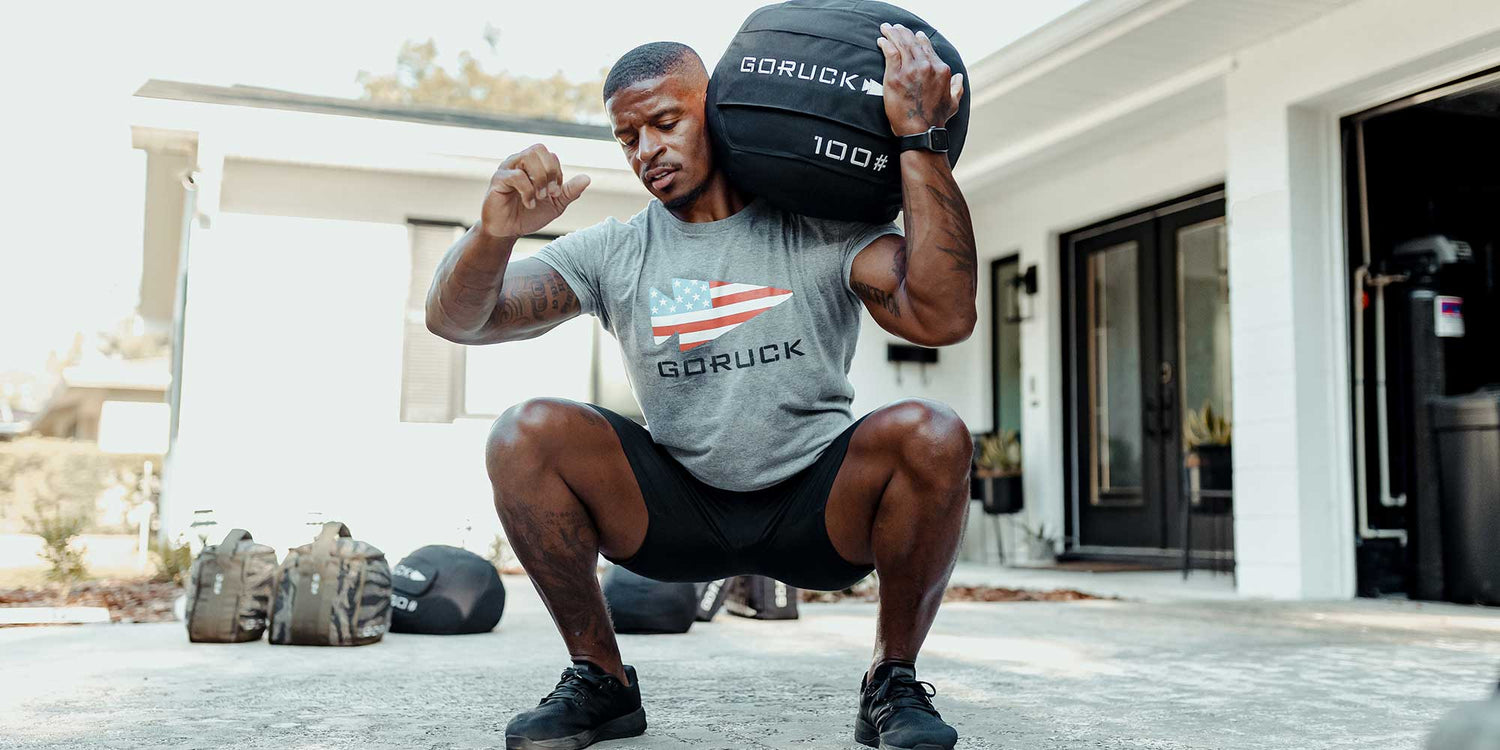 Man training outdoors with GORUCK sandbag, wearing GORUCK t-shirt and black shorts