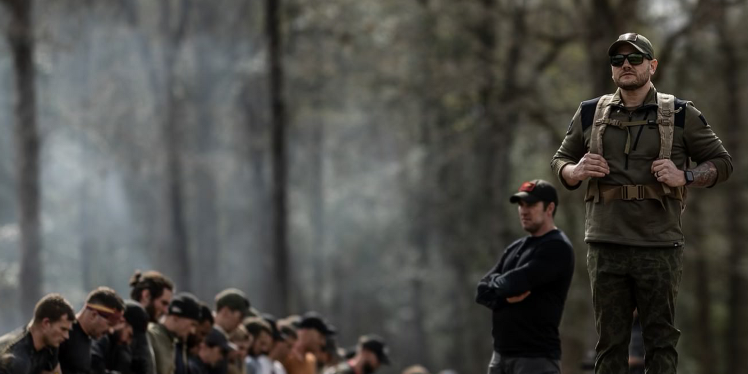 GORUCK rucking leader with backpack stands in forest, group training event outdoors