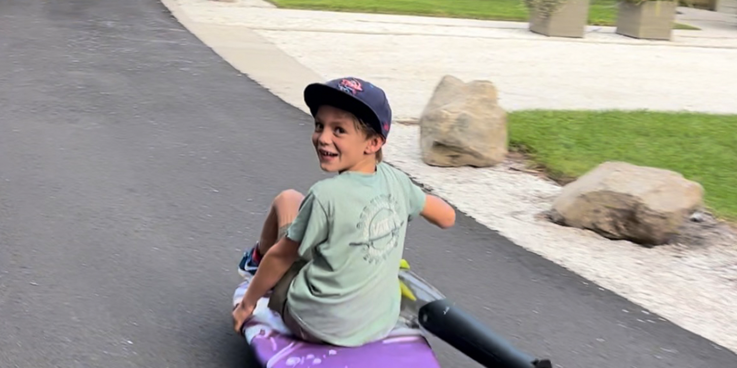 Smiling boy in cap riding a board on paved path outdoors, GORUCK lifestyle adventure scene