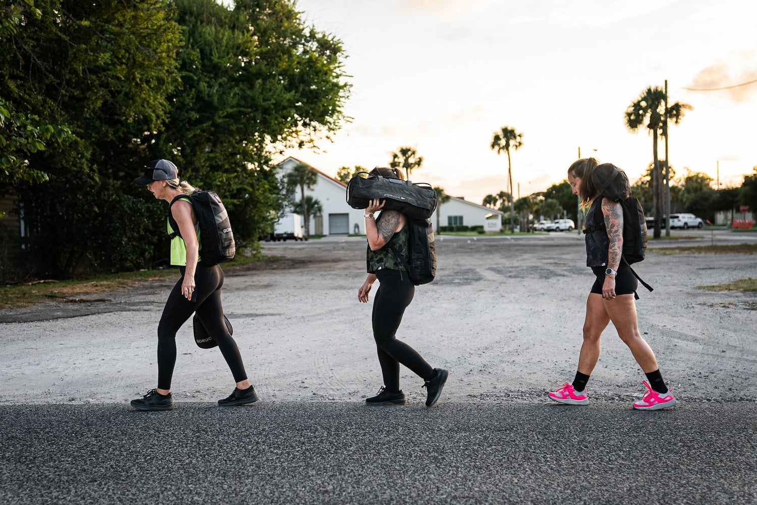 Three women rucking outdoors with GORUCK backpacks and gear at sunset