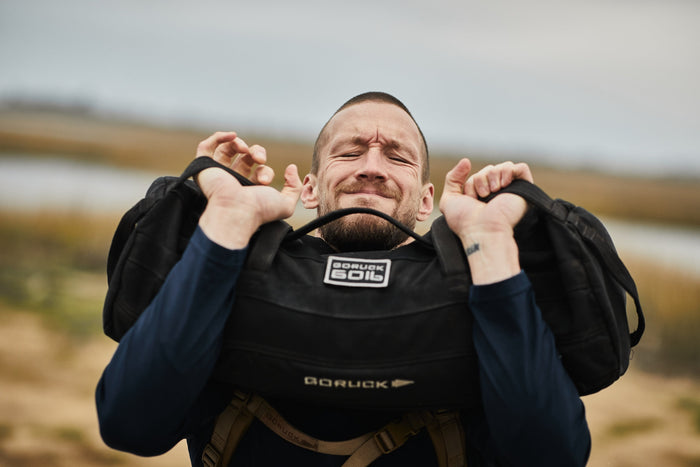 Man lifting GORUCK 60lb sandbag outdoors, showcasing tough rucking gear in action