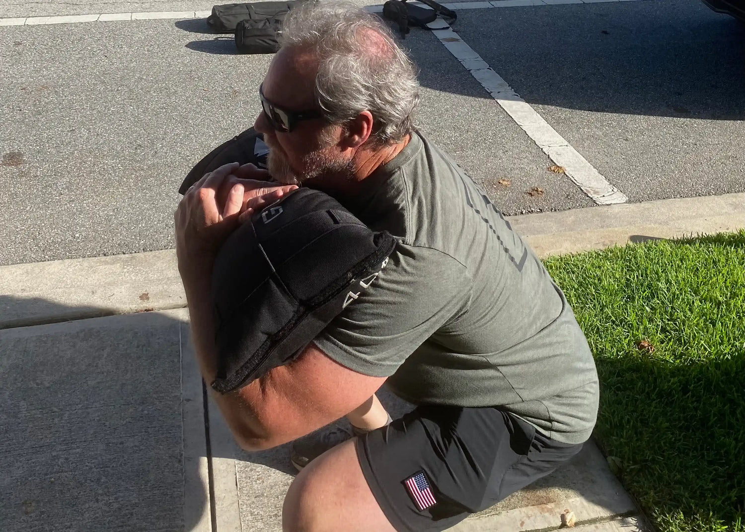 Man doing outdoor squat with GORUCK sandbag, wearing GORUCK gear and American flag shorts