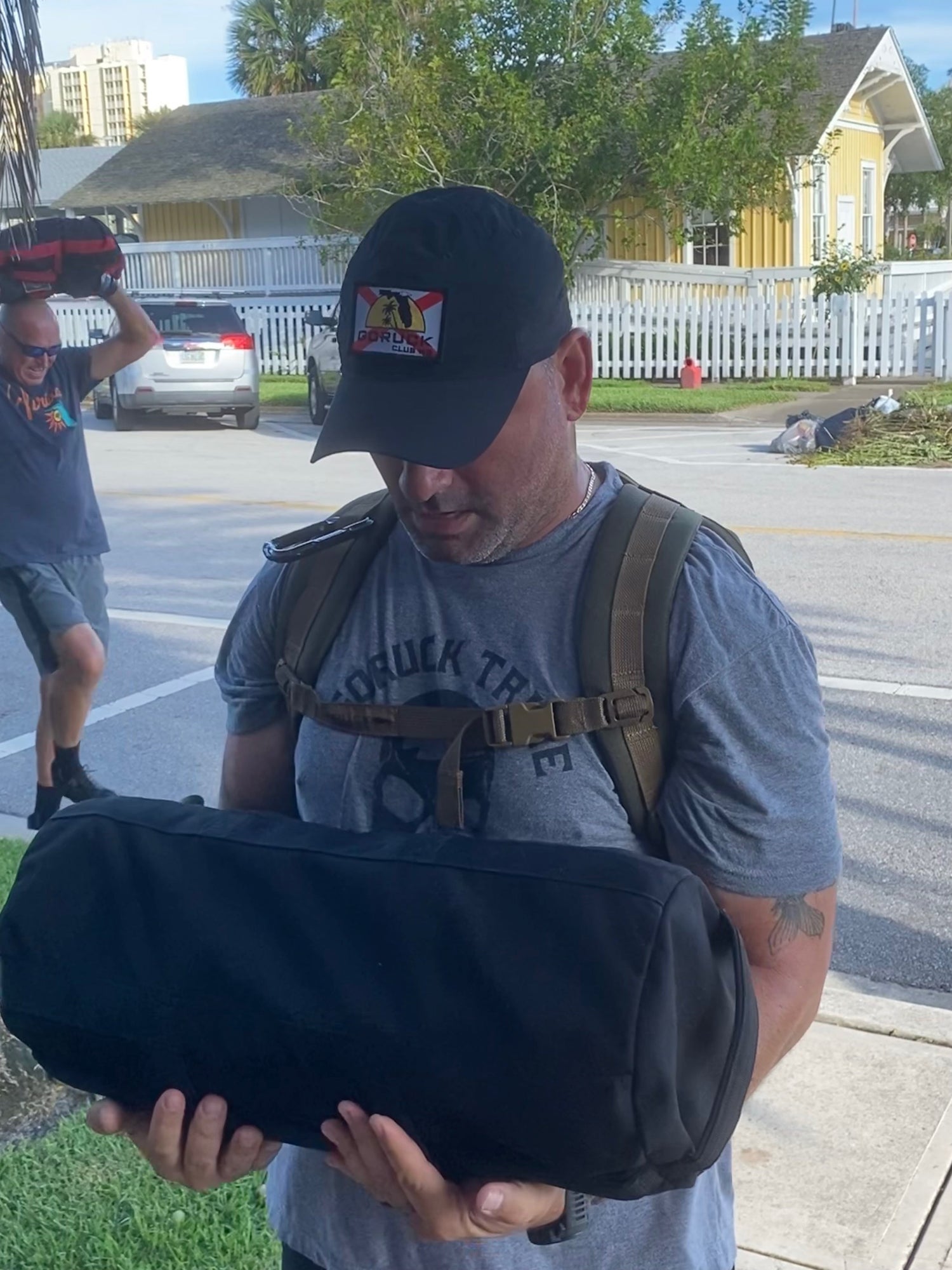 Man in GORUCK gear carrying weighted sandbag outdoors, participating in rucking event
