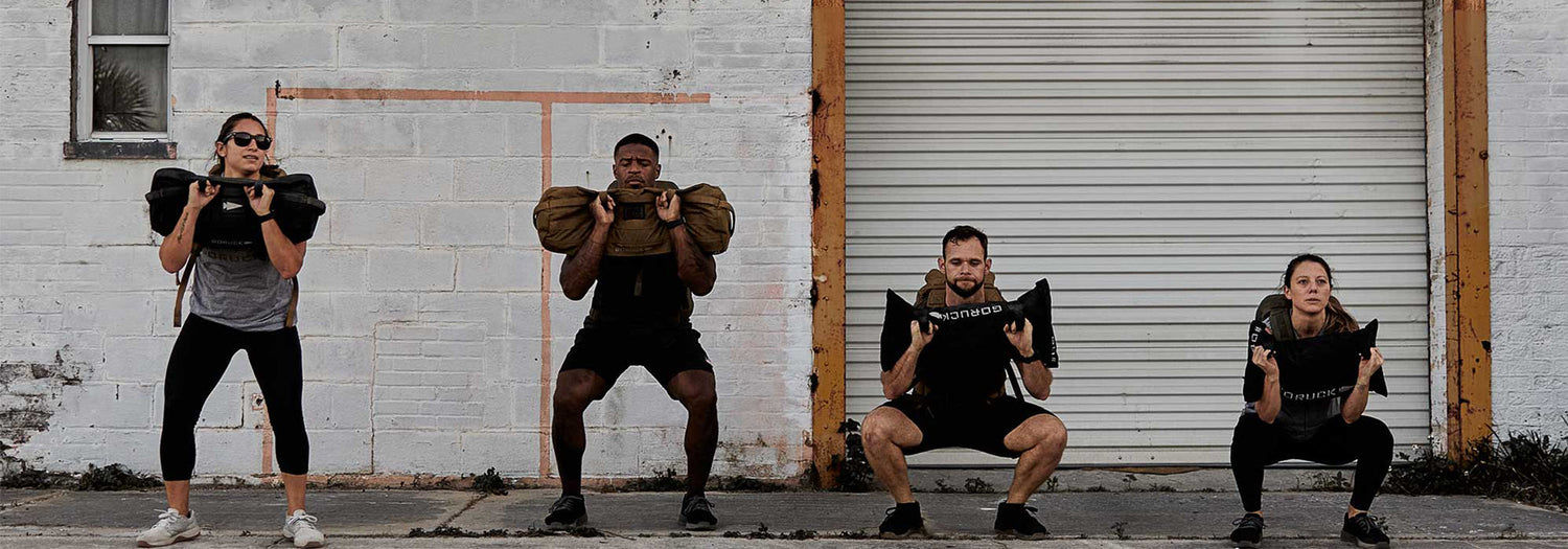 Group of four people squatting with GORUCK weighted sandbags in outdoor rucking workout