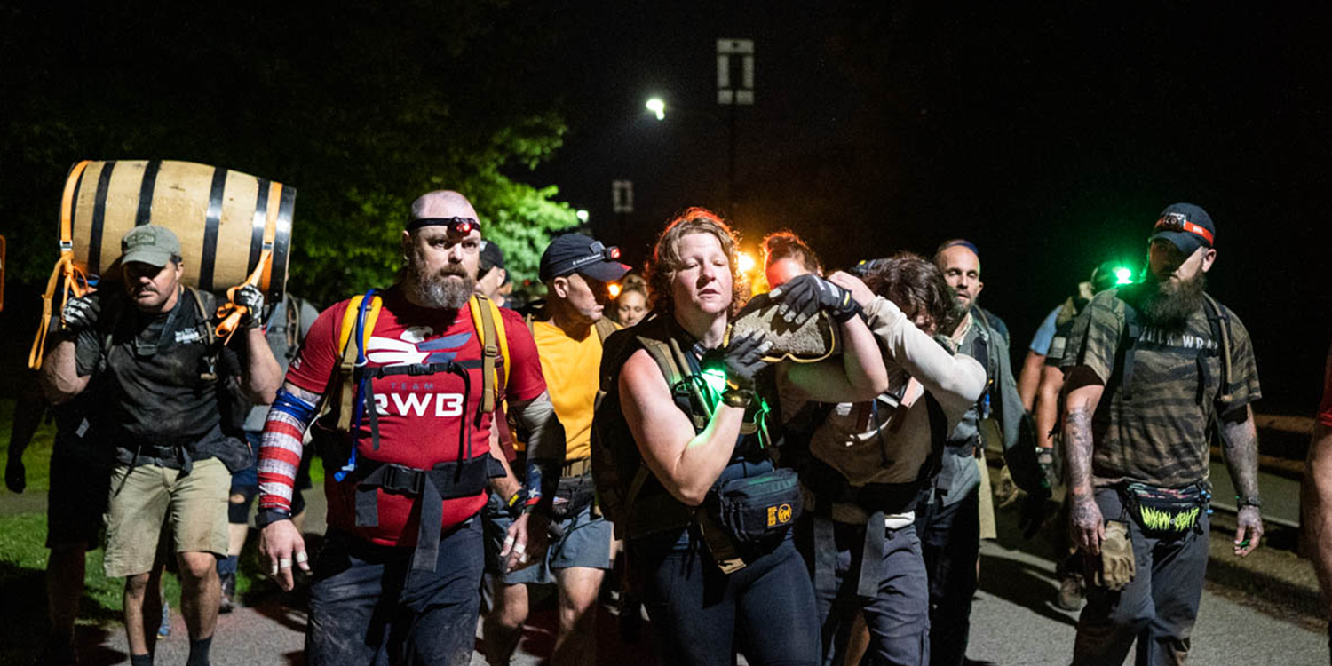 GORUCK event participants rucking at night, carrying gear and teamwork challenges outdoors