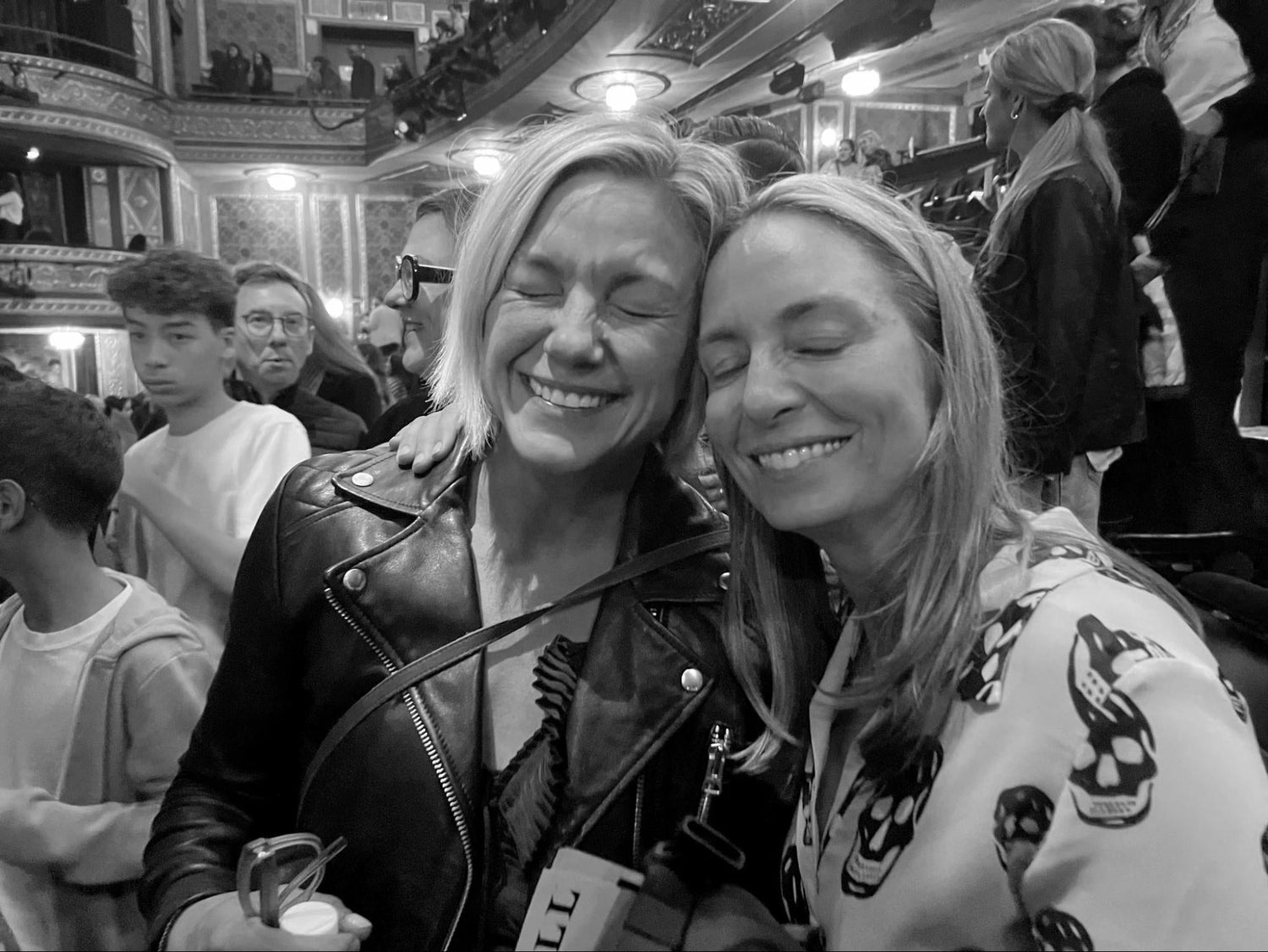 Two women smiling with eyes closed in a crowded theater, GORUCK event atmosphere