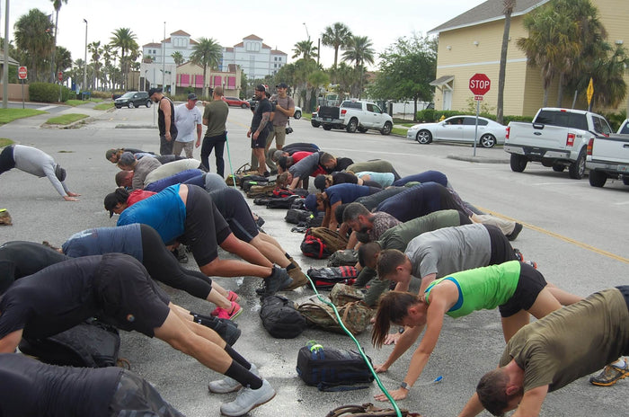GORUCK event participants doing outdoor group exercise with rucksacks on a city street