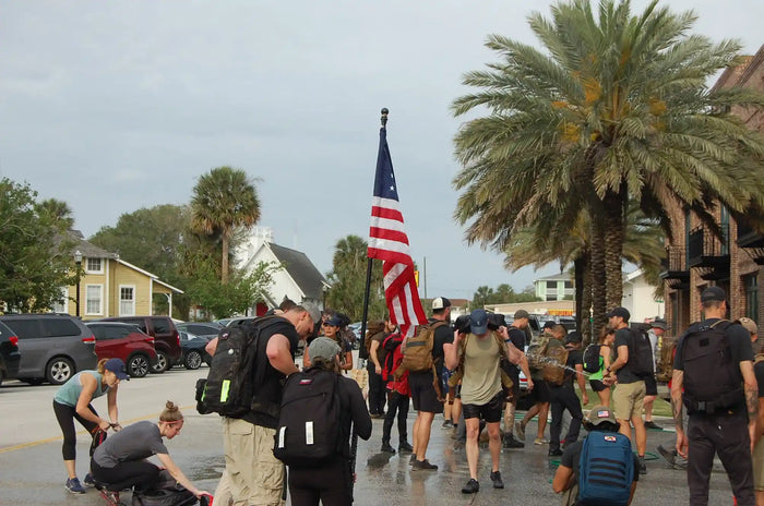 Group rucking event with GORUCK gear, American flag, and palm trees in urban setting